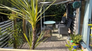 A patio with a table and chairs, a palm plant, and a hanging planter. - The Pheasant's Nest (Malvern)