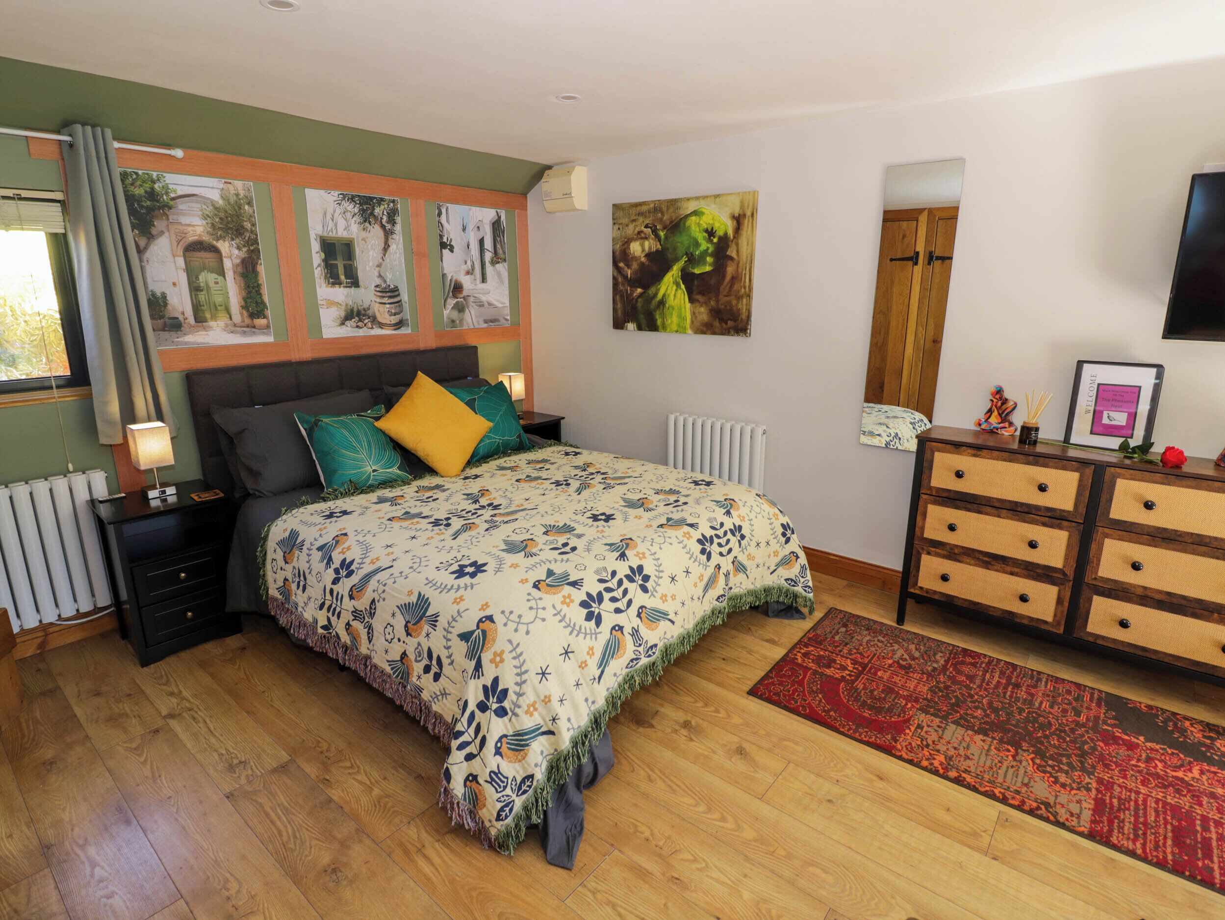 A bedroom with a bed, nightstands, a dresser, a radiator, and artwork on the walls.
