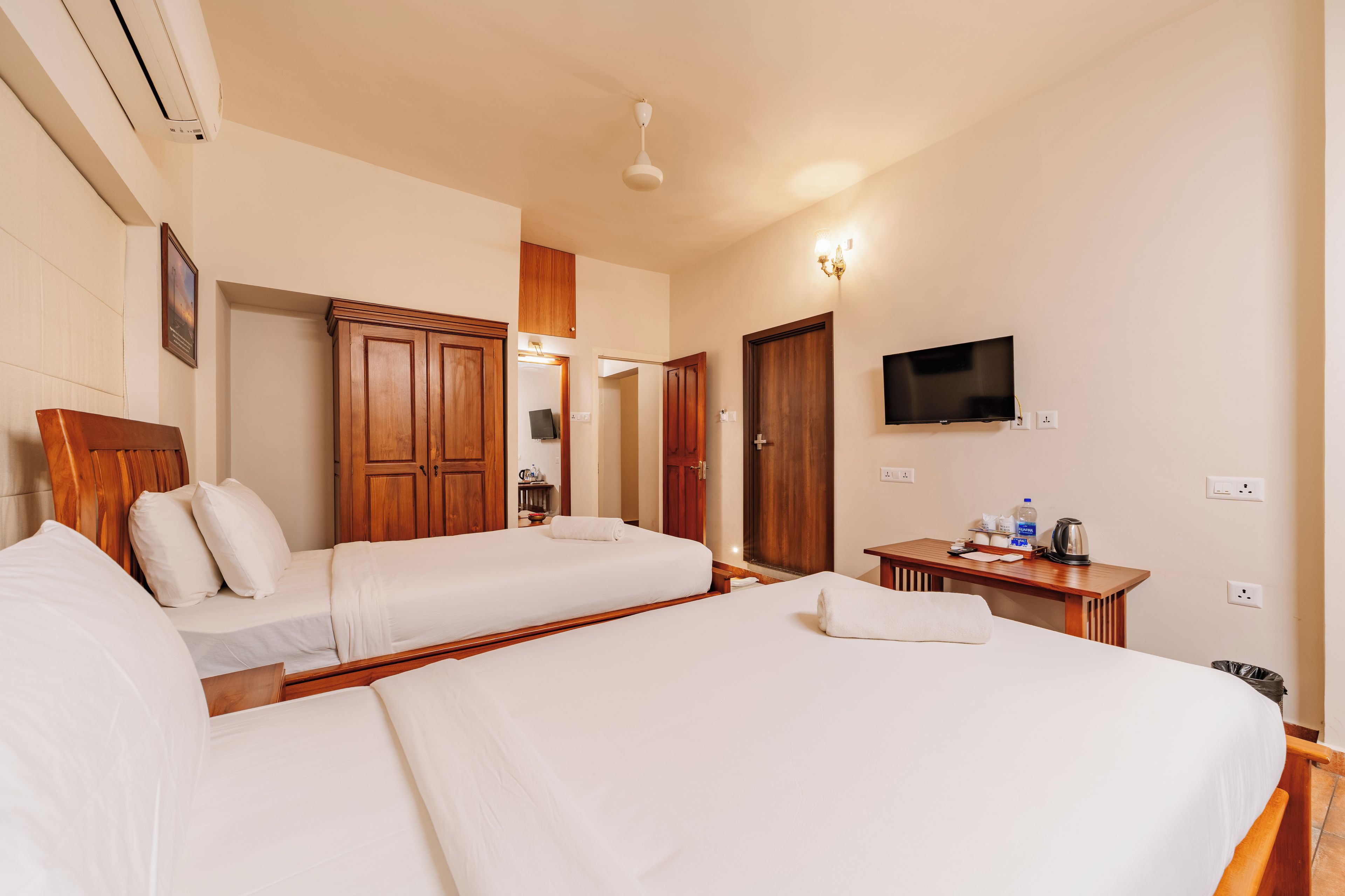 A hotel room with two beds, a TV, a desk with a kettle, and a framed picture on the wall.