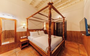 A four-poster bed with a wooden frame and a headboard, a nightstand with a mirror, and a wall-mounted lamp.
