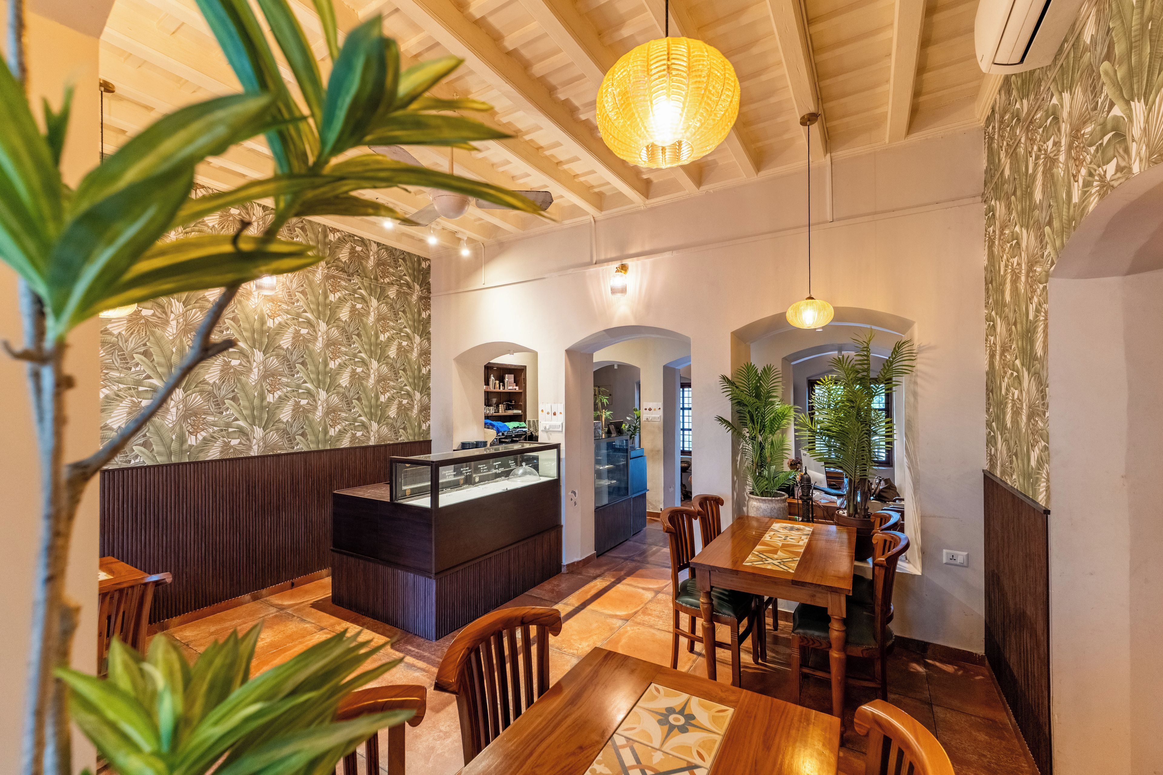 A restaurant interior with a wooden dining area, a counter with a display case, and tropical wallpaper.