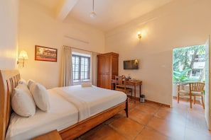 A hotel room with a bed, a desk with a chair, a television, and a window with curtains. - Sarada Mandiram A Heritage Hotel (Kanayannur)