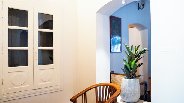 A dining area with a wooden table and chairs, a potted plant, and a window with a view of the outside. - Sarada Mandiram A Heritage Hotel (Kanayannur)