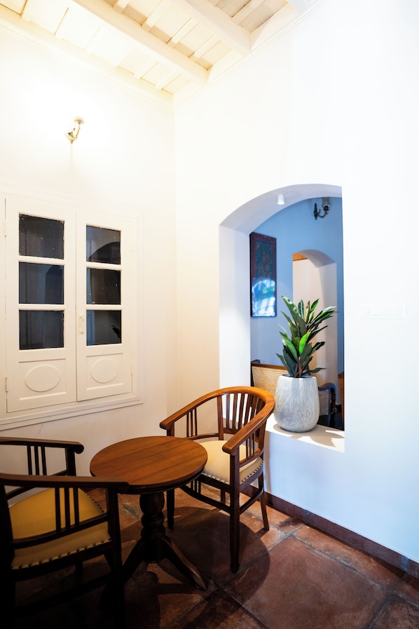 A dining area with a wooden table and chairs, a potted plant, and a window with a view of the outside. - Sarada Mandiram A Heritage Hotel (Kanayannur)