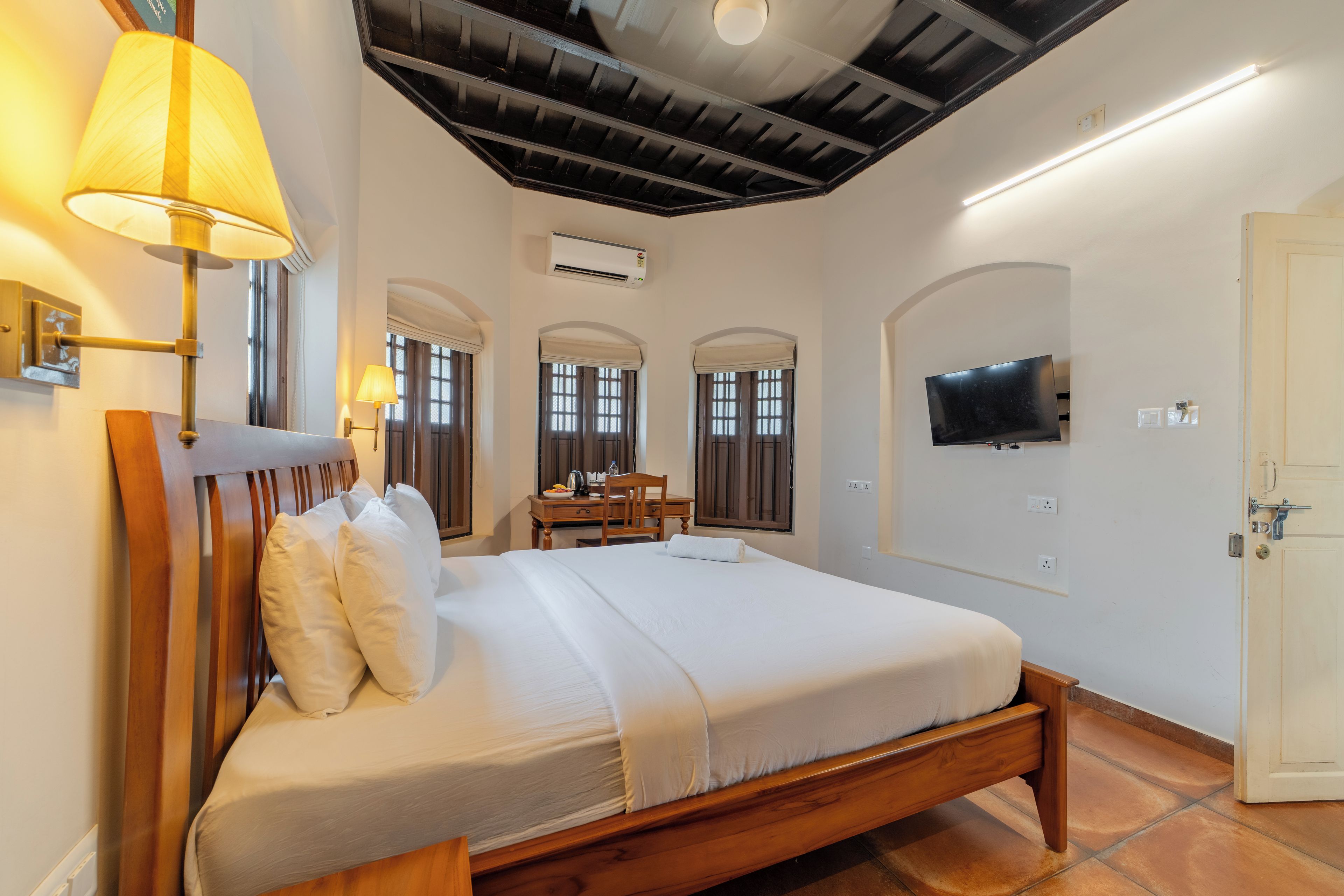 Une chambre d’hôtel avec un lit en bois, un bureau, une chaise, une télévision et un appareil de climatisation.