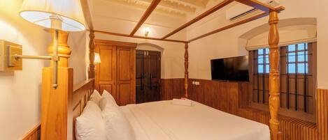 A four-poster bed with white linens, wooden headboard, and a wall-mounted lamp.