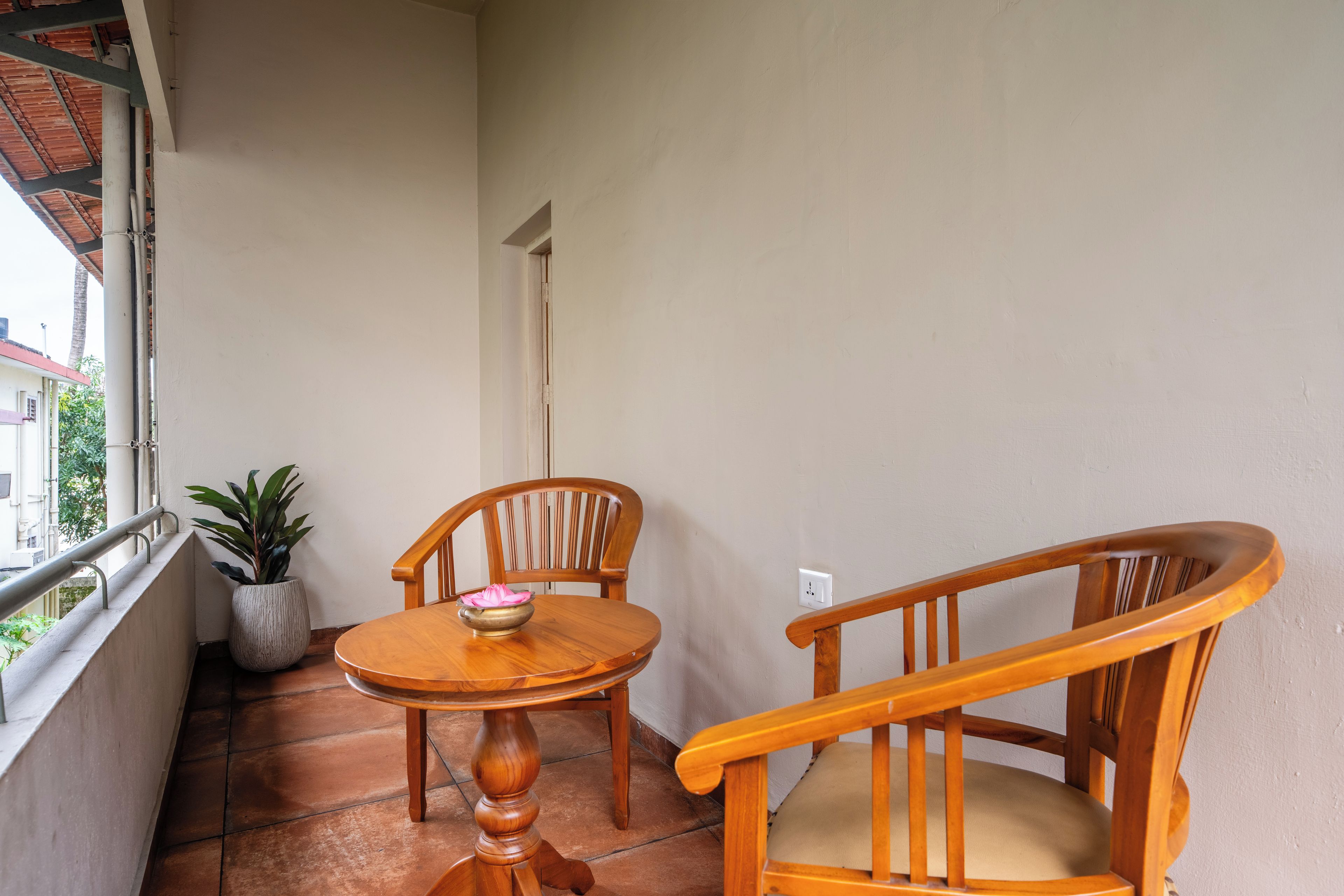 Un balcone con un tavolo di legno, due sedie, una pianta in vaso e vista sugli edifici.