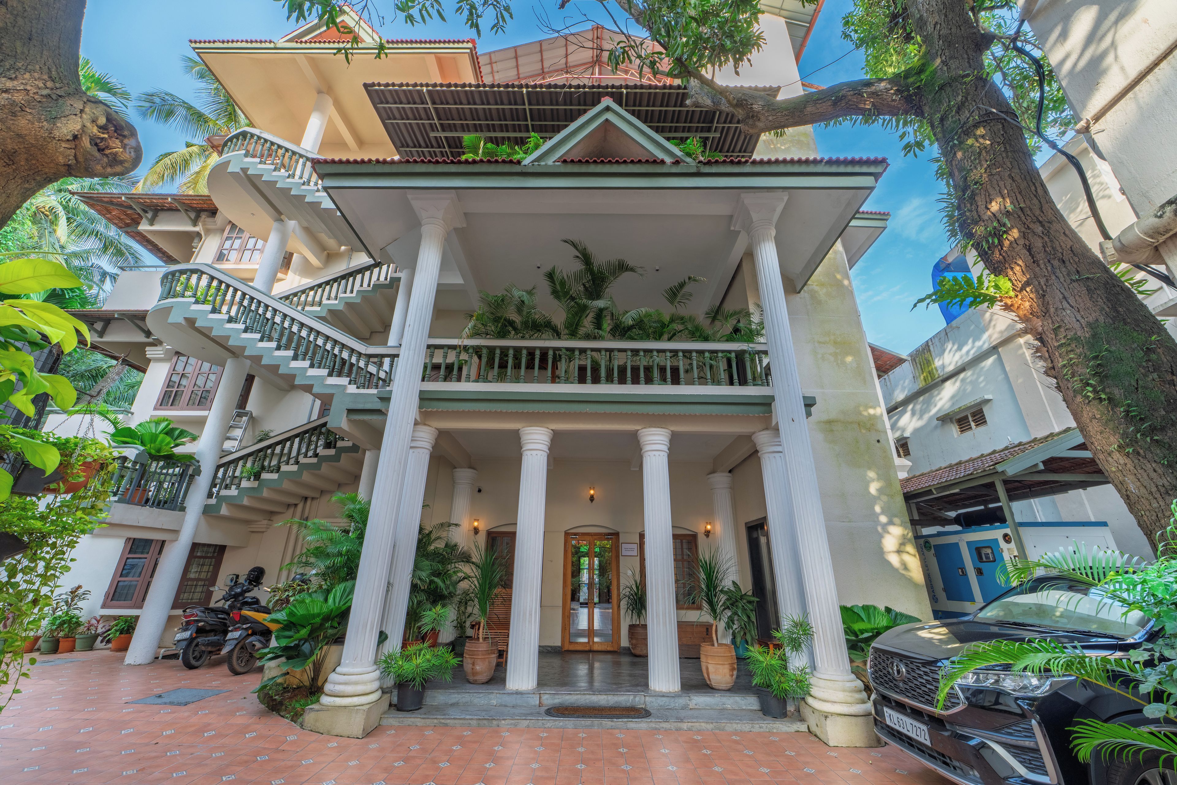 A multi-story building with a central entrance flanked by columns, a staircase, and potted plants.