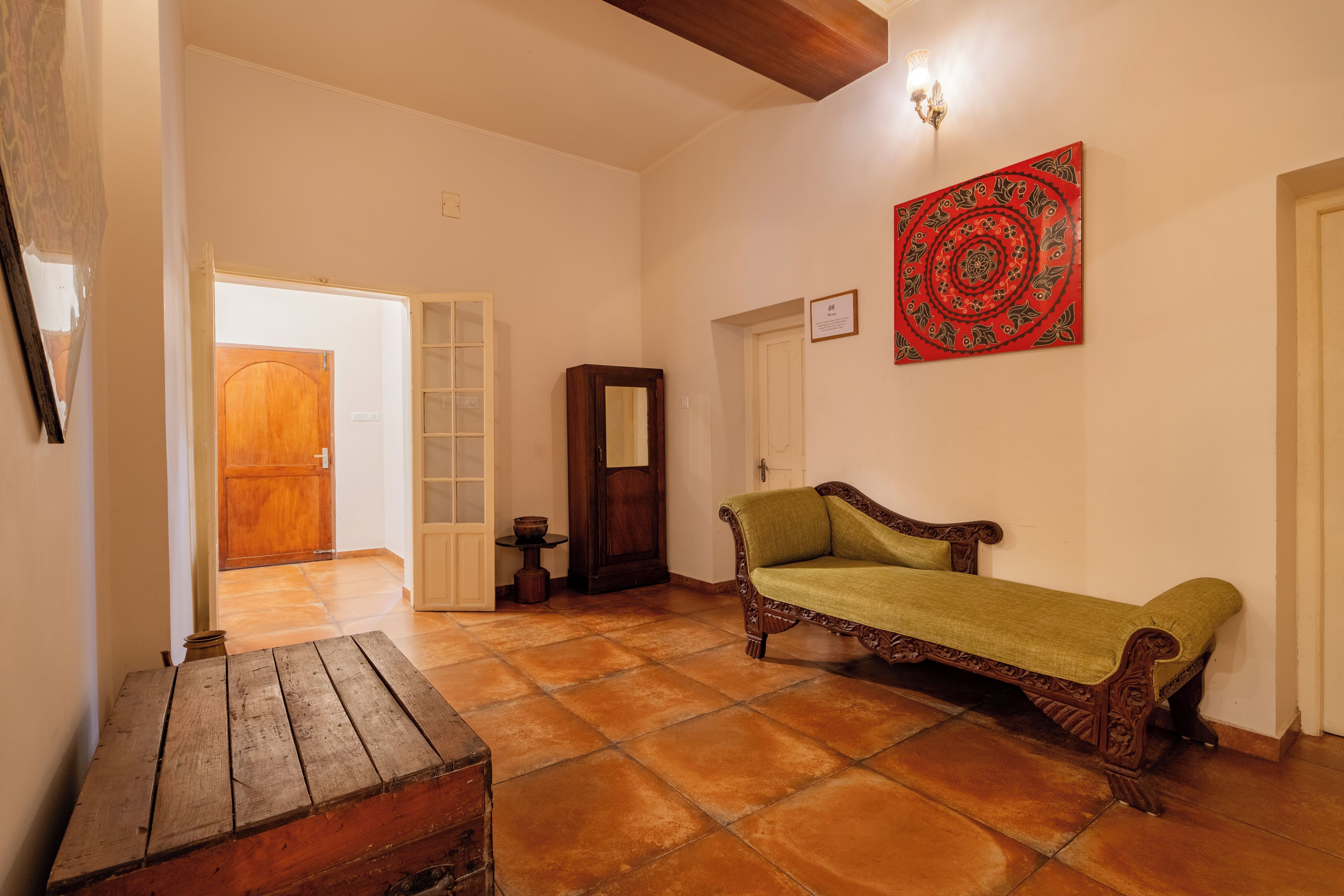 Una habitación con un banco de madera, un sofá verde, un armario de madera y un tapiz rojo con estampado.