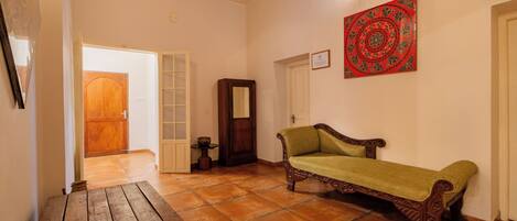 Una habitación con un banco de madera, un sofá verde, un armario de madera y un tapiz rojo con estampado.