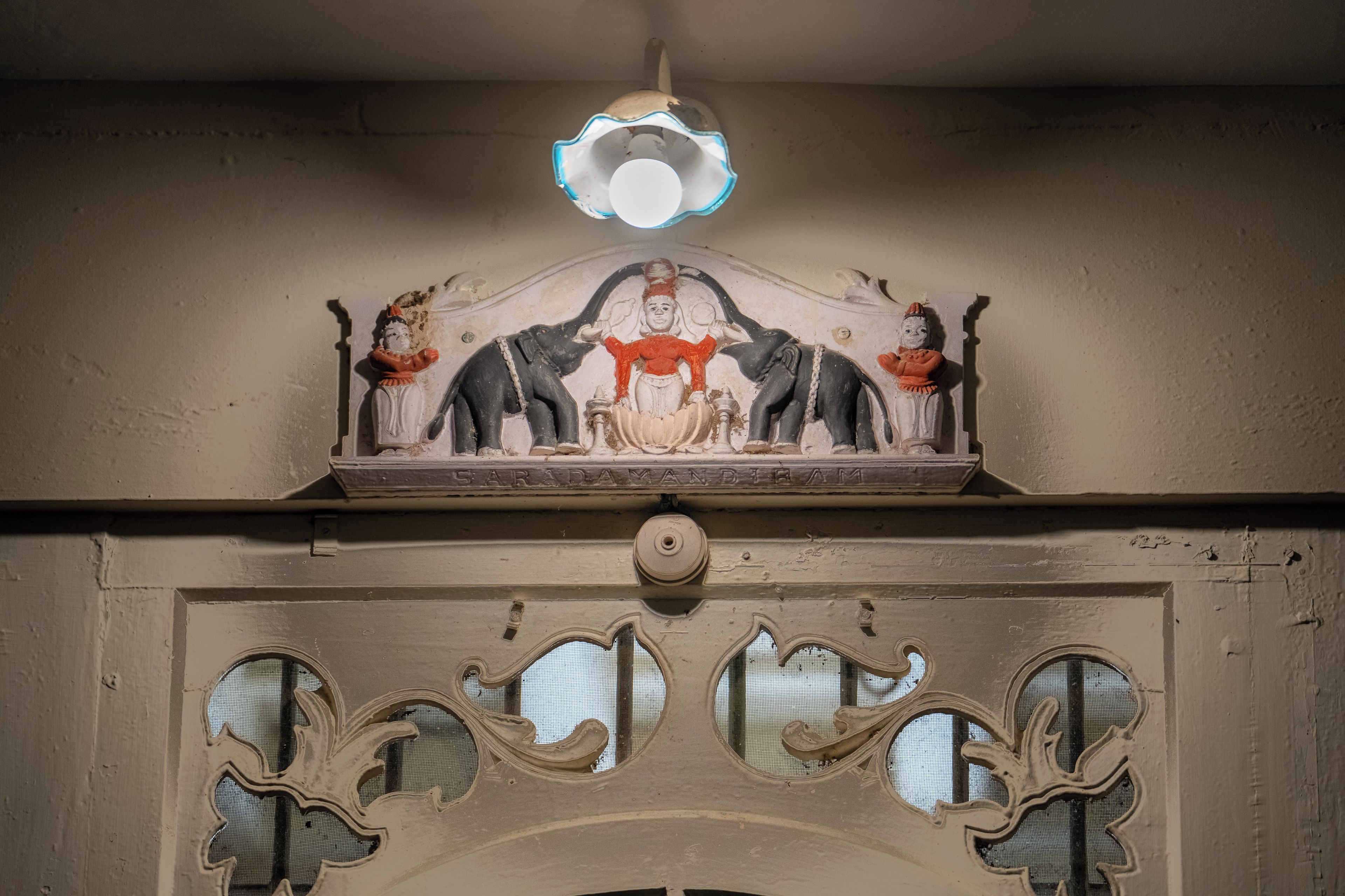 A ceiling with a decorative sculpture featuring elephants and a central figure. Below, there is a textured wall with a series of circular cutouts.
