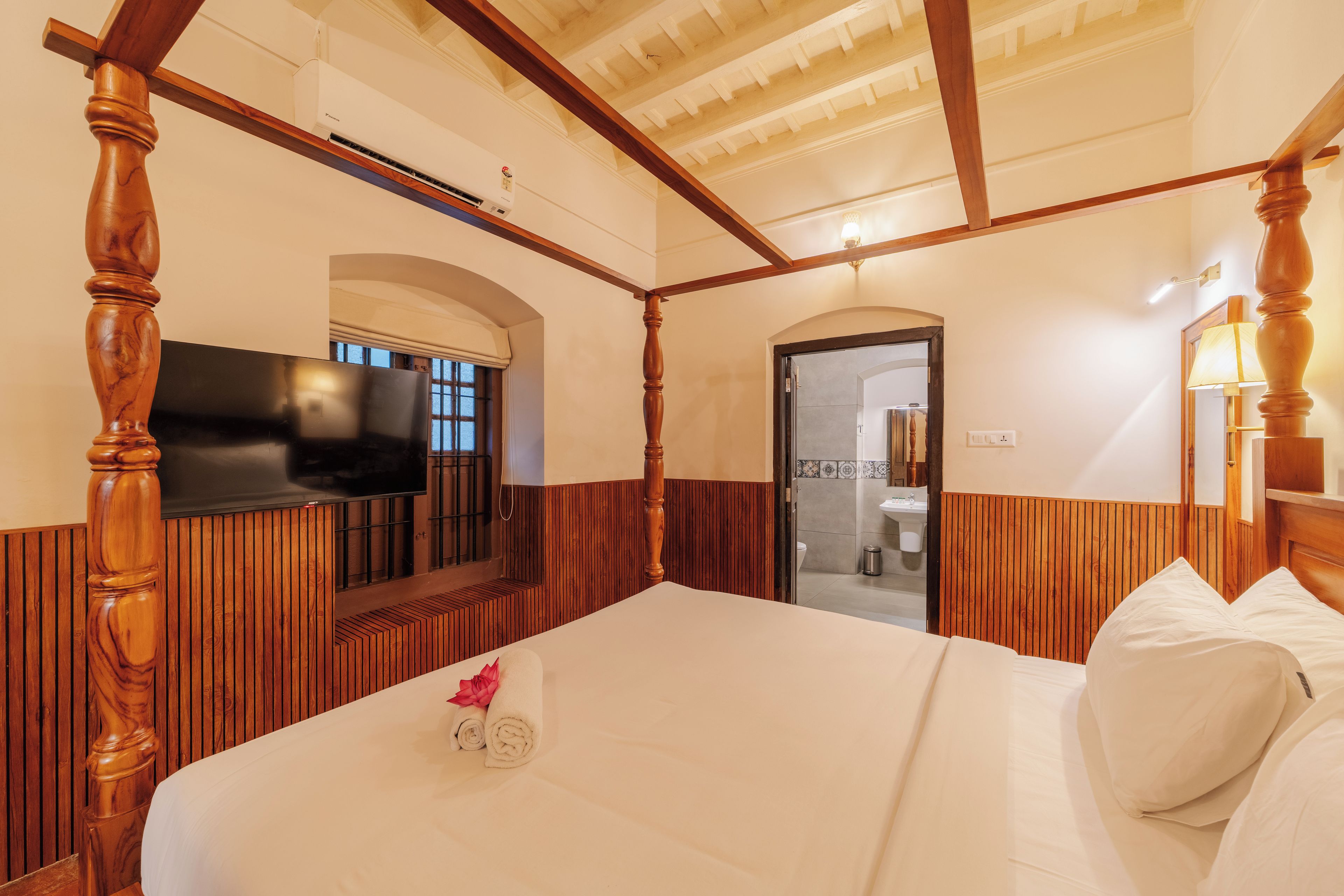 A hotel room with a large bed, wooden headboard, a flat-screen TV mounted on the wall, and a wooden ceiling.