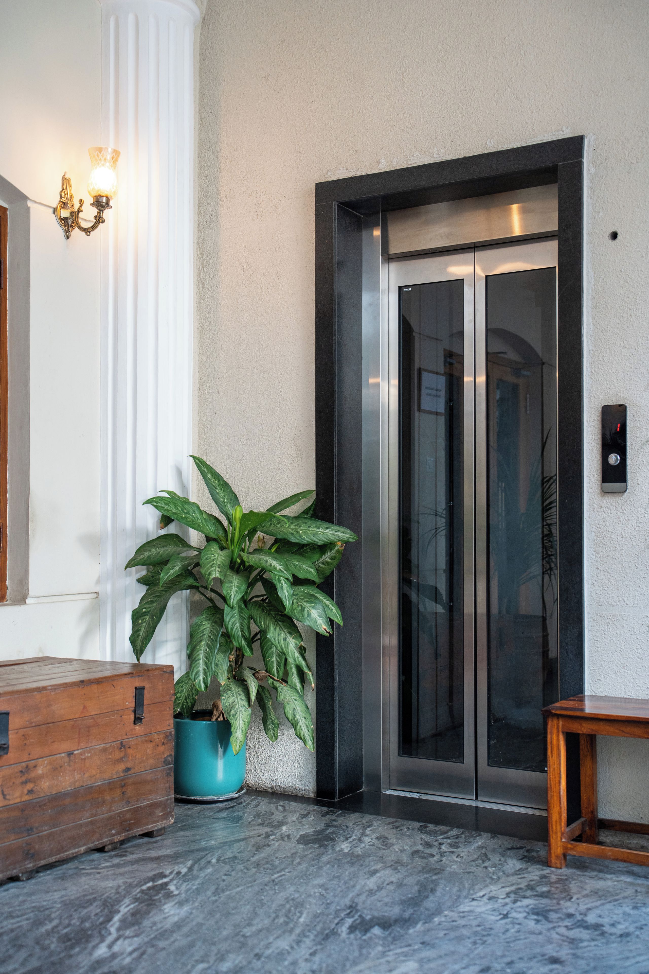 An elevator with a metallic finish, a potted plant, and a wooden bench.