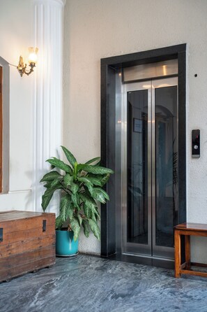 An elevator with a metallic finish, a potted plant, and a wooden bench. - Sarada Mandiram A Heritage Hotel (Kanayannur)