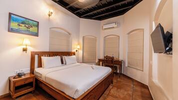 Habitación de hotel con cama de madera, lámparas de noche, escritorio con silla, unidad de aire acondicionado y televisor montado en la pared.