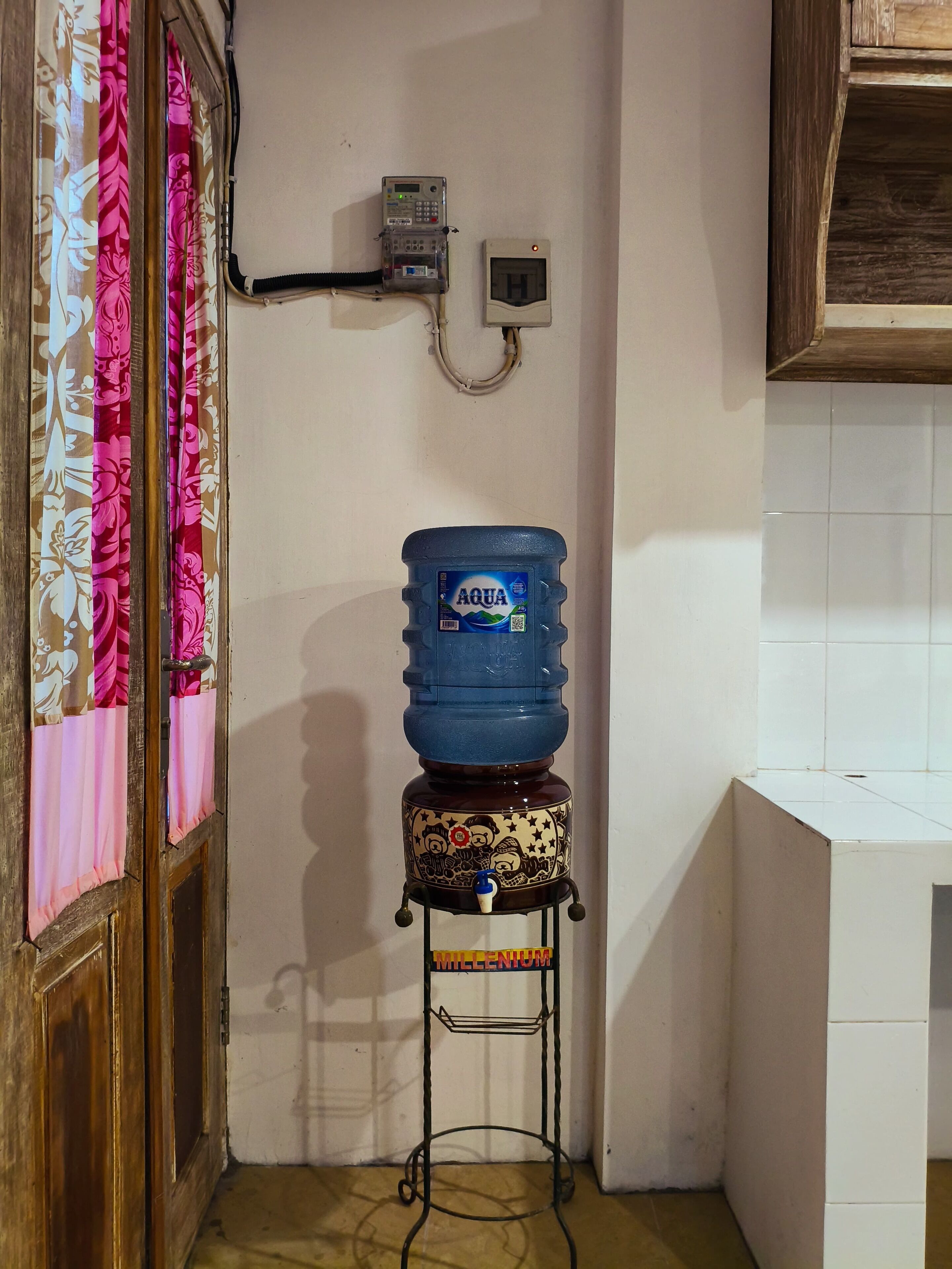 A water dispenser on a stand, a wall-mounted phone, and a door with floral curtains.