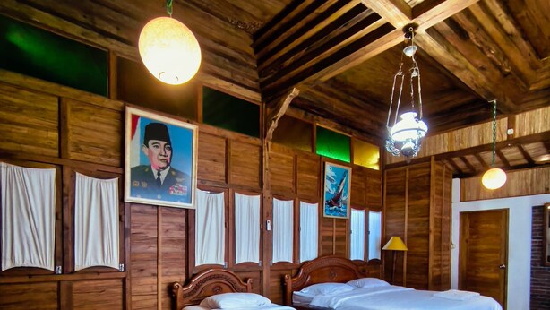Una stanza in legno con tre letti, un soffitto in legno e un ritratto appeso al muro.