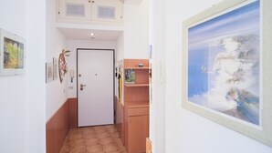 Um corredor com uma porta branca, um pequeno armário de madeira e um quadro na parede.