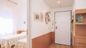Quarto de hotel com duas camas, uma porta e um pequeno armário de madeira.