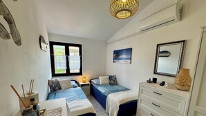 Ein Schlafzimmer mit zwei Betten, einem Schminktisch, einem Fenster mit Spitzenvorhängen, einem Gemälde und einem Spiegel.