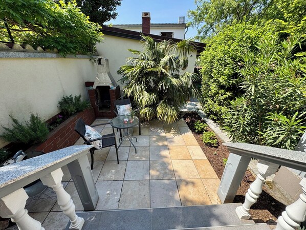 A patio area with a table and chairs, surrounded by plants and a brick wall. - Apartment Evelyn (Jadranovo)