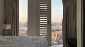 A hotel room with a large bed, a TV, and a view of a cityscape through a sliding door.