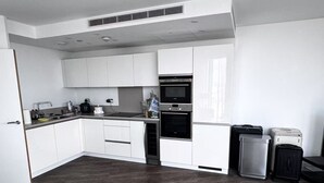 A modern kitchen with white cabinets, a built-in oven, and a microwave. There is a dining area with a glass table and a black chair.