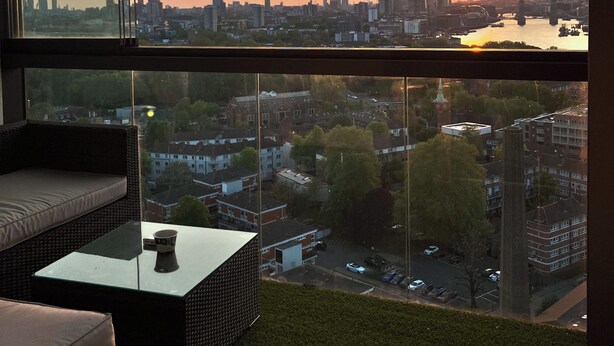 A modern room with a large window overlooking a cityscape at sunset.