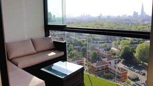 A modern living room with a sofa and a glass coffee table, offering a view of a cityscape with buildings and trees.