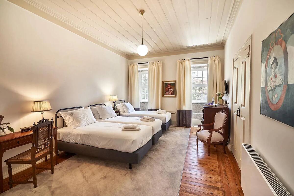 A bedroom with two beds, a desk, a chair, and a painting on the wall.