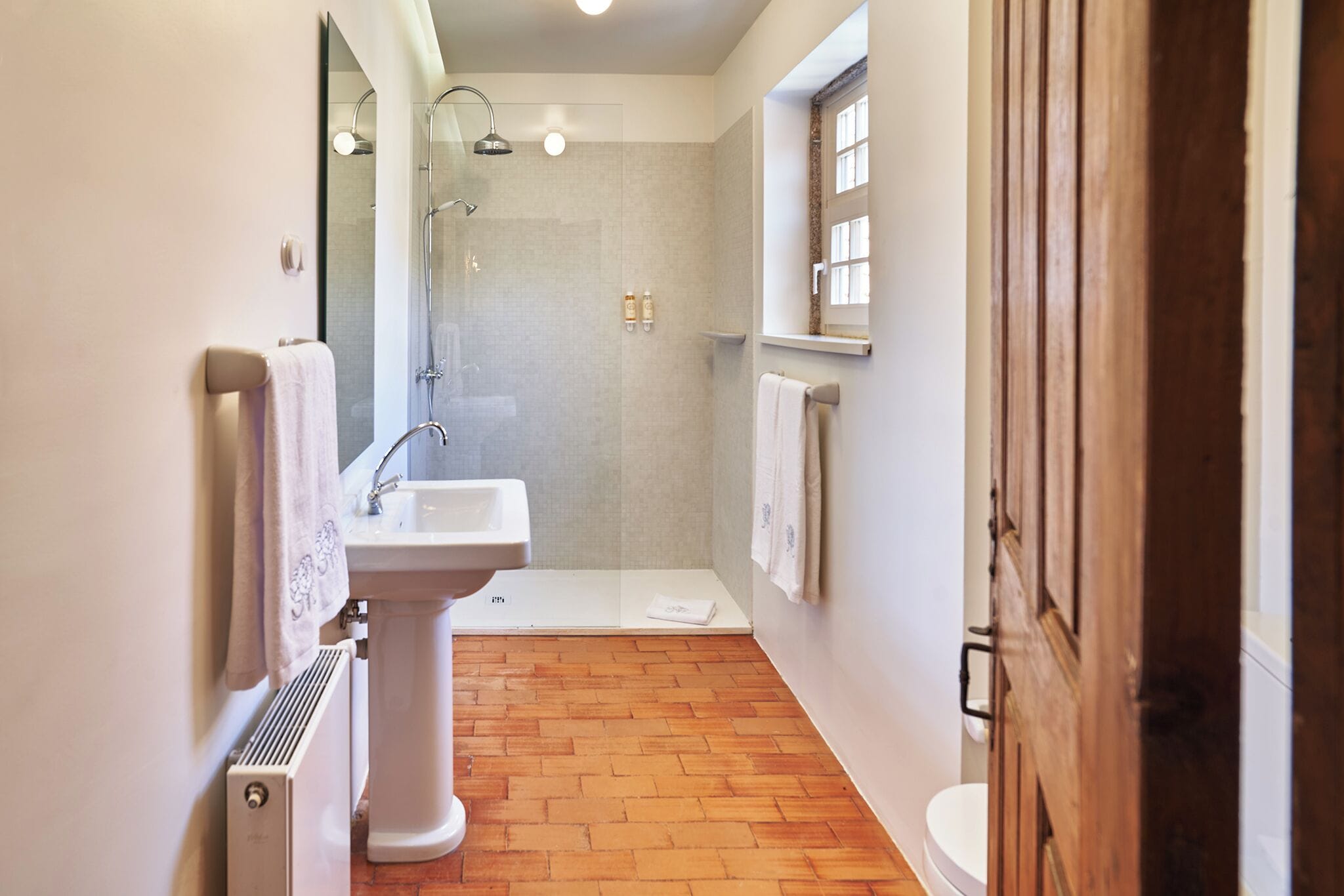 A modern bathroom with a pedestal sink, a glass-enclosed shower, and a wooden floor.