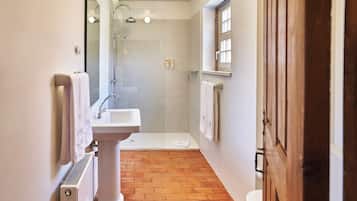 A modern bathroom with a pedestal sink, a glass-enclosed shower, and a wooden floor.
