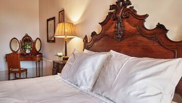 A neatly made bed with white linens, a wooden headboard with intricate carvings, a bedside table with a lamp, and a mirror on the wall.