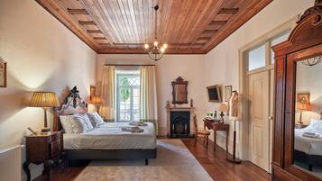 A bedroom with a wooden ceiling, a large bed, a fireplace, and a mirror.