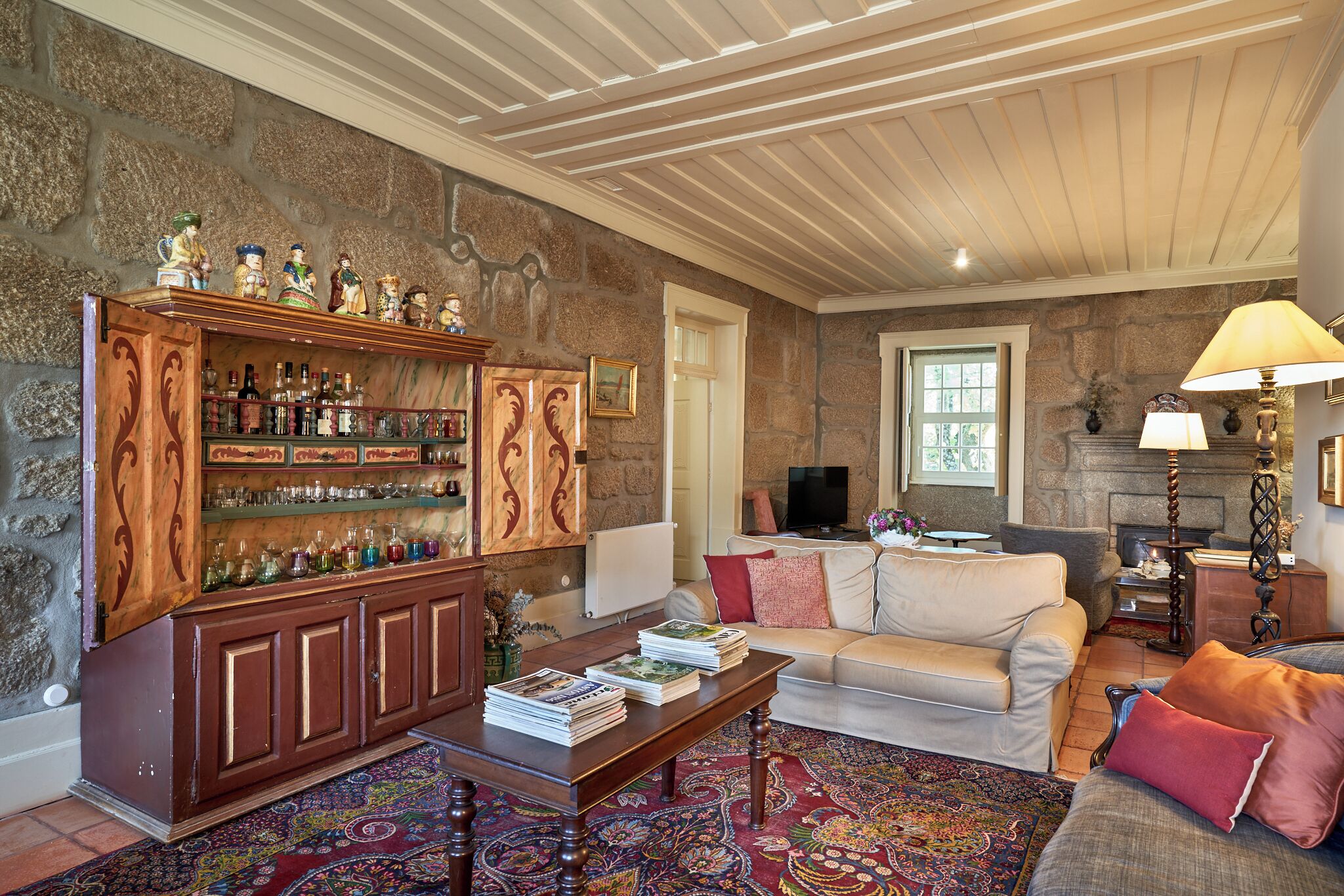 A cozy living room with a fireplace, a wooden cabinet with bottles, a sofa, and a coffee table.