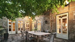 An outdoor patio with a stone wall, a wooden table, and chairs. - Solar de Vilar Seco (Nelas)