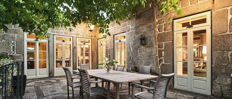 An outdoor patio with a stone wall, a wooden table, and chairs.