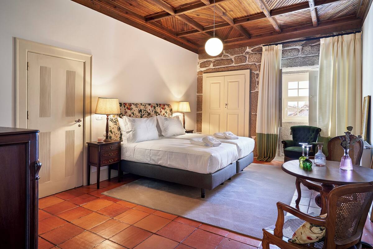 A bedroom with a bed, bedside tables, a dresser, a dining table with chairs, and a view of the outside.