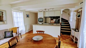 Zona pranzo con tavolo e sedie in legno, cucina sullo sfondo e una scala che conduce a un altro piano.