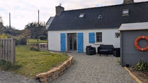 Una piccola casa con vialetto sterrato, recinzione in legno e muro di pietra.