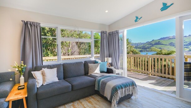 A cozy living room with a grey sofa, a wooden side table, and a view of a scenic landscape through large windows.