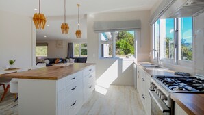 A modern kitchen with a central island, pendant lights, and a view of greenery outside.