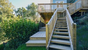 A wooden staircase leading to a deck with a view of a house and surrounding greenery.