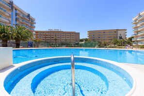 A swimming pool with a diving board, surrounded by palm trees and hotel buildings in the background.