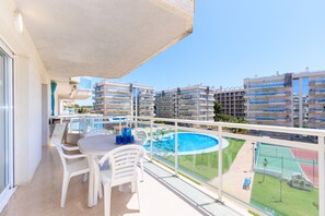 A balcony with a table and chairs, overlooking a swimming pool and adjacent buildings.
