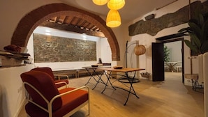 A cozy living room with a red sofa, a wooden dining table, and a stone wall. - At Di Toni's house, for families and groups (Castiglion Ubertini)