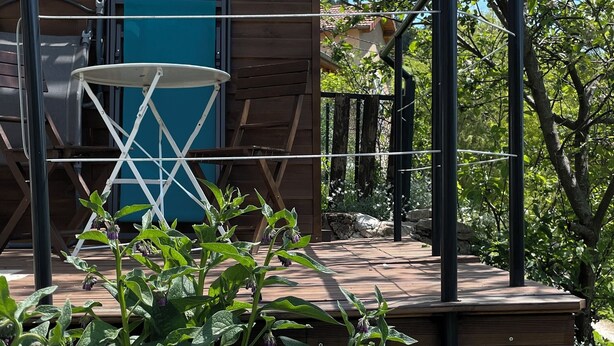 Una cabaña de madera con puerta azul, una terraza de madera y barandilla metálica.