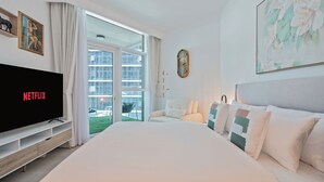Habitación de hotel moderna con una cama grande, un televisor mostrando 'NETFLIX', un balcón con vistas a edificios y un cuadro en la pared.
