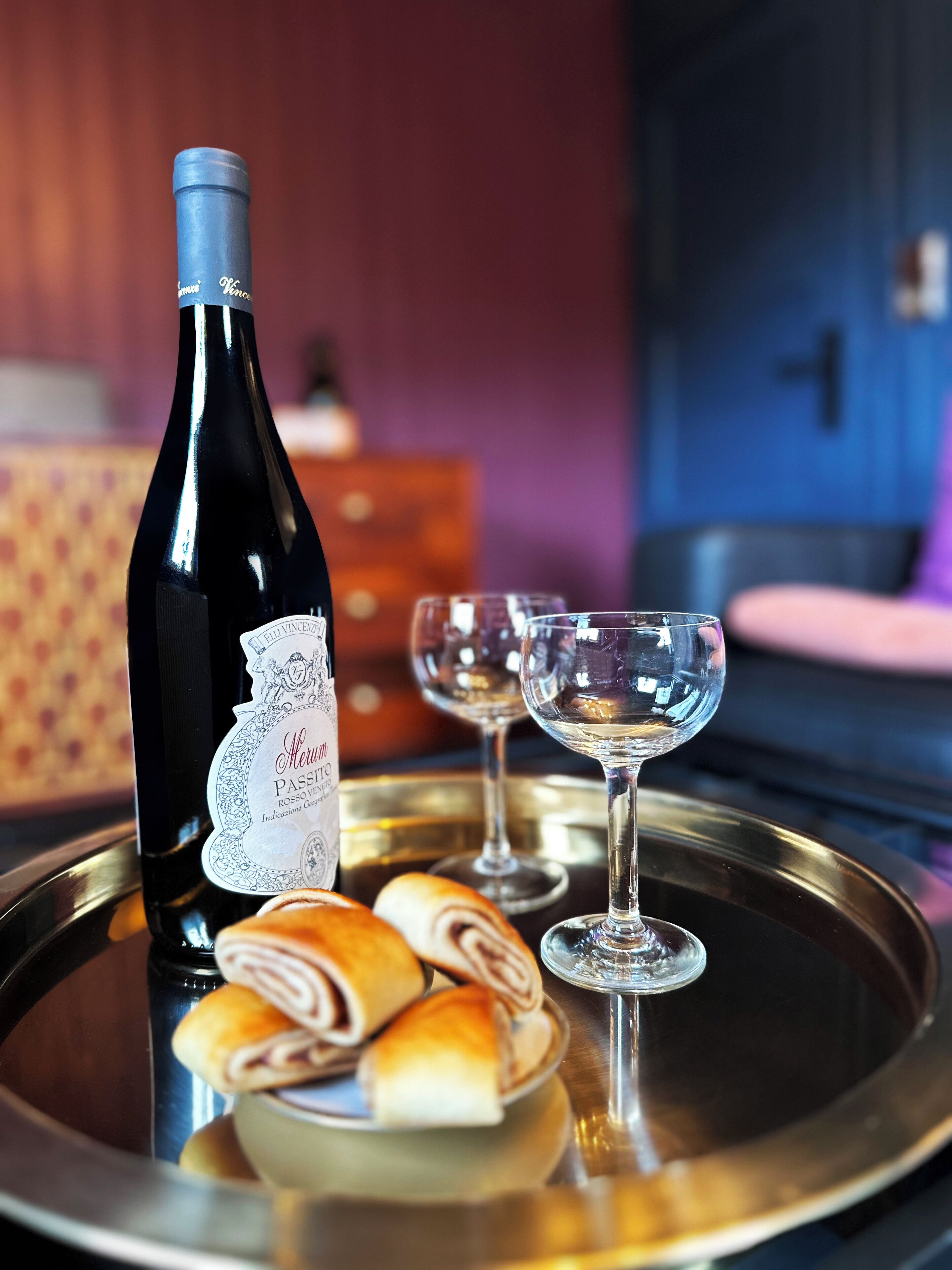 A bottle of wine, two wine glasses, and a tray with pastries on a reflective surface.