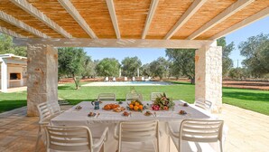 An outdoor dining area with a table set for four, surrounded by stone pillars, under a wooden pergola. - My Rental Homes - Trulli Heaven with private pool and large garden (San Michele Salentino)